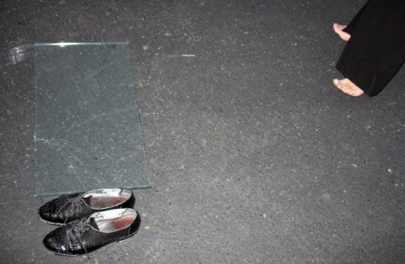 Schwarze Schuhe liegen auf dem Boden neben einem zerbrochenen Glasstück.