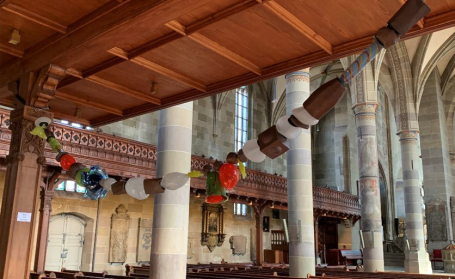 Bunte Holzfiguren hängen an Balken in einer alten Kirche.